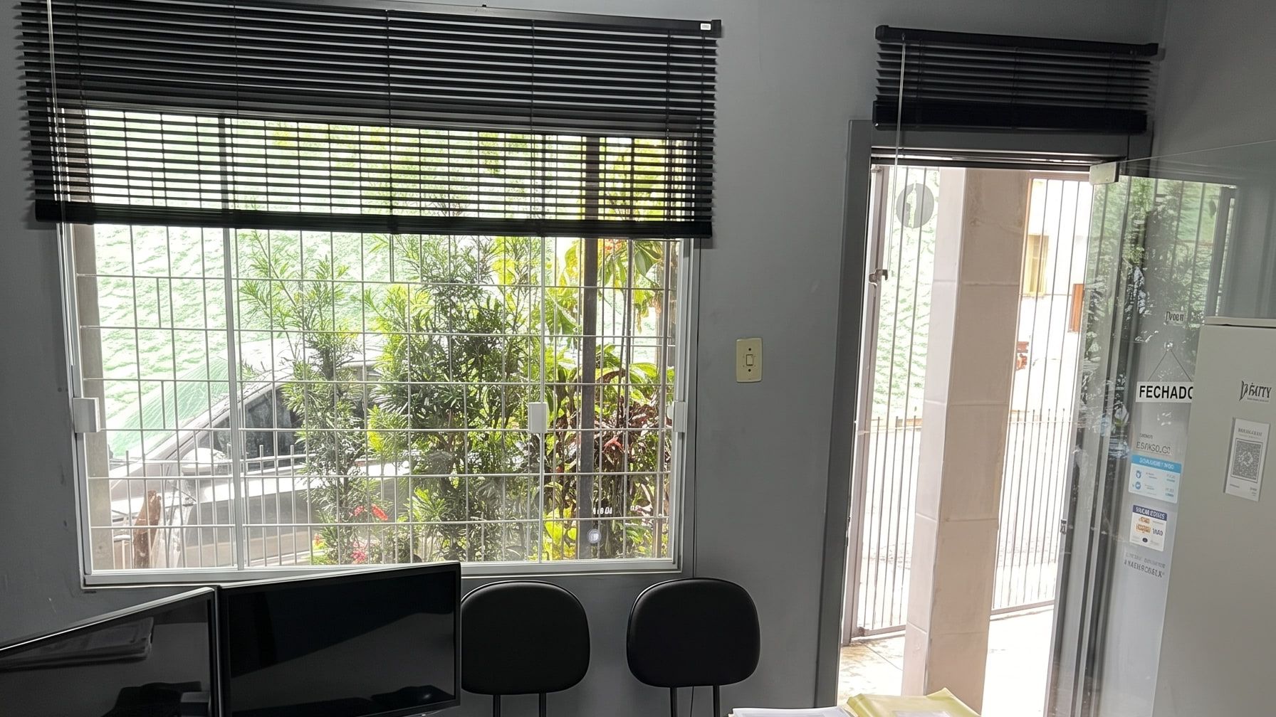 Sala do escritório da Nepack, com estações de trabalho junto à janela e a porta de entrada ao fundo